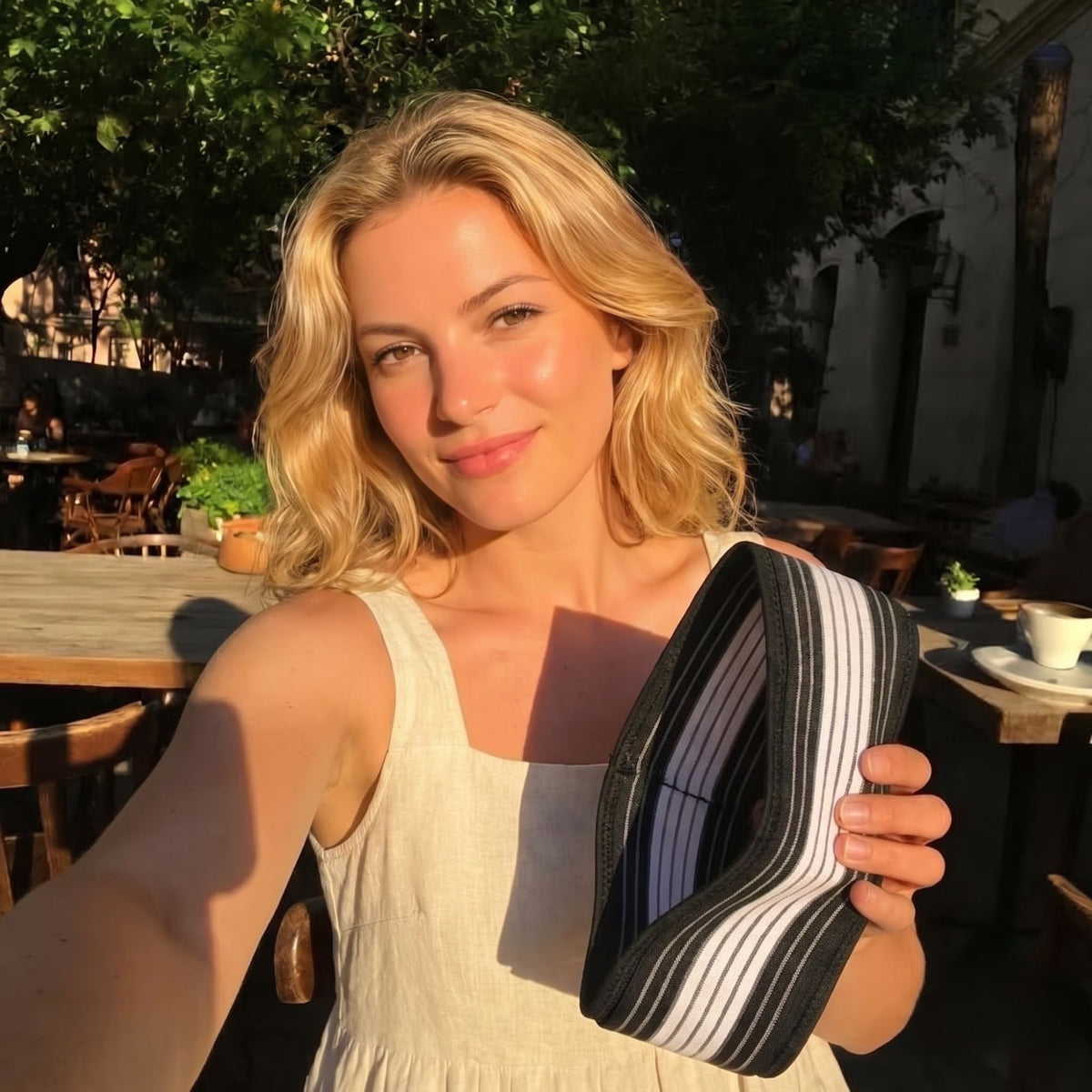 Woman at a sunny café table holding up the striped pelvic support belt